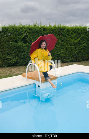 Femme en imperméable tipping toe en piscine Banque D'Images