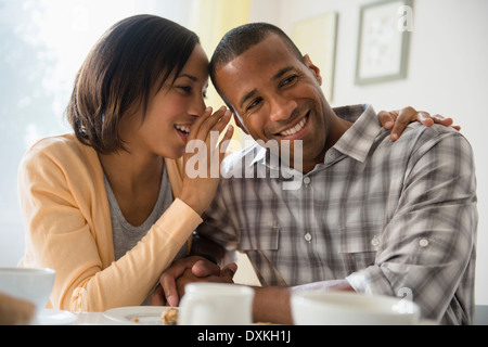 Femme chuchoter dans l'oreille de petit ami à table Banque D'Images