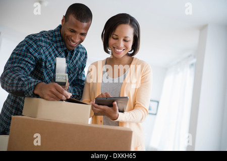 Couple with digital tablet taping up moving boxes Banque D'Images