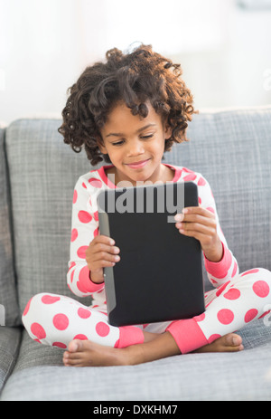 African American girl in pajamas using digital tablet on sofa Banque D'Images