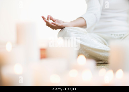 Hispanic woman meditating in lotus position près de bougies allumées Banque D'Images