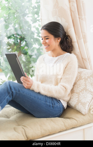 Hispanic woman using digital tablet au siège de fenêtre Banque D'Images