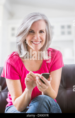 Portrait of smiling Caucasian woman text messaging on sofa Banque D'Images