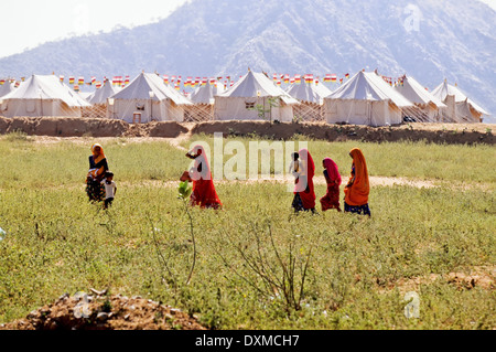 Groupe de femmes indiennes marche à travers champs en face d'tentes à Pushkar camel fair, Inde Banque D'Images
