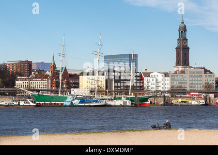 L'homme est assis sur la plage en face de l'bateau musée Rickmer Rickmers et Eglise Saint-Michel de Hambourg en Allemagne. Banque D'Images