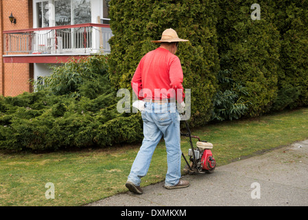 Bordure de trottoir le long de la pelouse l'homme avec la machine à essence Honda. Banque D'Images