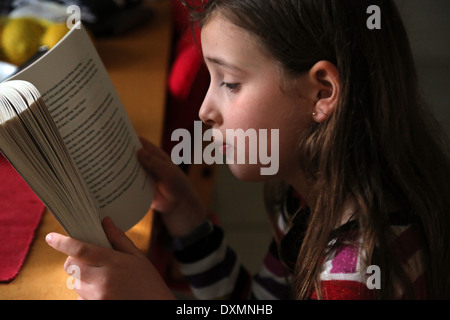 9 ans, fille, assis à table de cuisine La lecture d'un livre Ruby Redfort Surrey England Banque D'Images