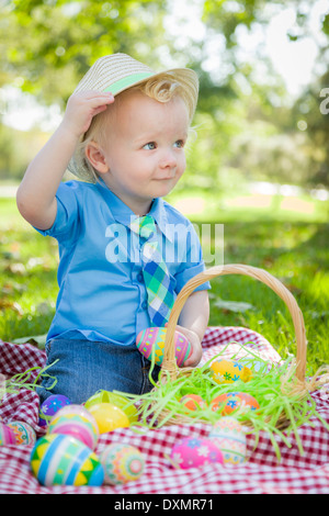 Adorable petit garçon à l'extérieur on Picnic Blanket Holding Easter Eggs Astuces son chapeau. Banque D'Images