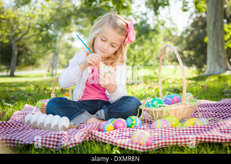 Cute Young Girl Coloring joyeusement ses oeufs de Pâques avec le pinceau dans le parc. Banque D'Images