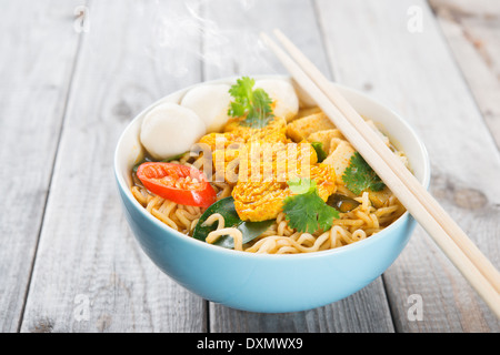 Curry épicé nouilles potage instantané avec des baguettes sur la table à manger en bois. Chaud, cuit à la vapeur avec de la fumée. Banque D'Images