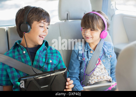 Happy brother and sister avec des écouteurs à l'aide de digital tablets in back seat of car Banque D'Images