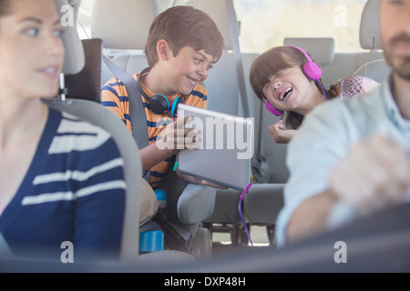 Happy brother and sister using digital tablet in back seat of car Banque D'Images