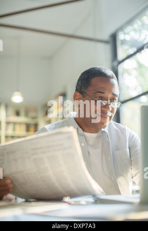 Senior man reading newspaper and using laptop Banque D'Images