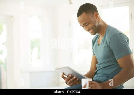 Smiling man drinking coffee and using digital tablet Banque D'Images