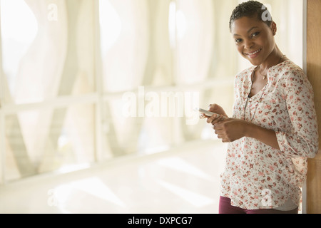 Portrait of smiling woman text messaging with cell phone in corridor ensoleillé Banque D'Images