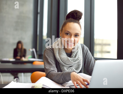 Happy young woman sitting in la bibliothèque avec des livres et un ordinateur portable à rechercher des informations pour ses études. Banque D'Images
