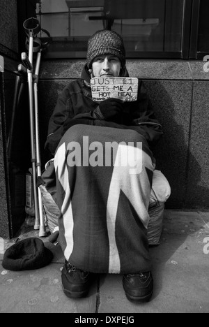 Sans-abri avec un panneau dans les rues de Londres avec une paire de béquilles à côté de lui. Banque D'Images