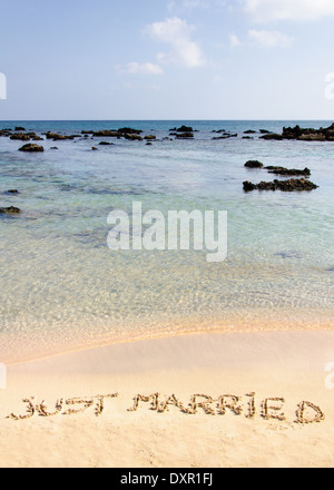 Récemment Mariés écrit dans le sable sur une belle plage, les vagues bleu clair en arrière-plan Banque D'Images