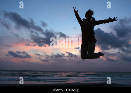 Adopter une grille, États-Unis d'Amérique, silhouette, femme est de faire un saut dans l'air sur la plage au crépuscule Banque D'Images