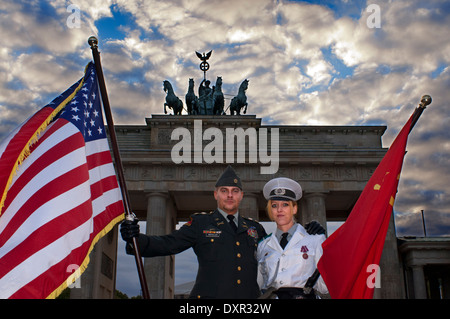 Acteurs habillés comme des soldats américains et soviétiques posent pour des photos avec les touristes devant la porte de Brandebourg à Berlin. Drapeaux Banque D'Images