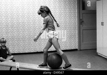 Berlin, DDR, petite fille augmente en éducation physique sur un banc sur un ballon Banque D'Images