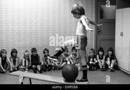 Berlin, DDR, petit garçon s'élève en éducation physique sur un banc sur un ballon Banque D'Images