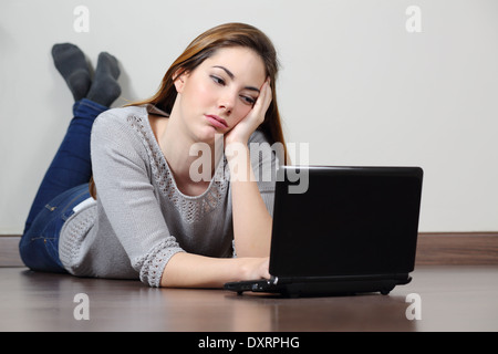 Ennuyer adolescentes parcourt les médias sociaux dans un ordinateur portable se trouvant sur le plancher à la maison. Banque D'Images