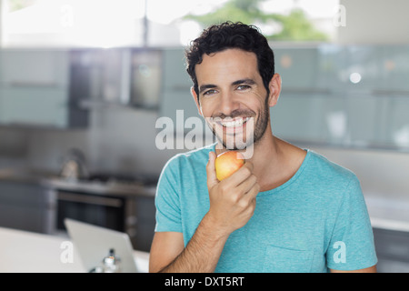 Portrait of smiling man eating apple en cuisine Banque D'Images
