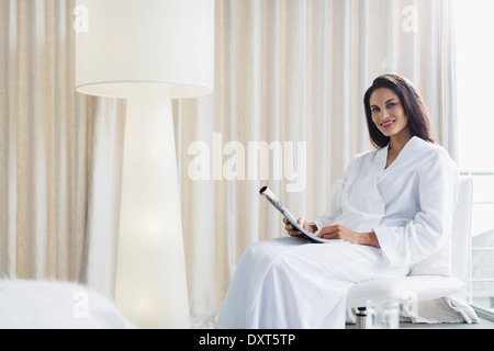 Portrait of smiling woman in bathrobe reading newspaper Banque D'Images