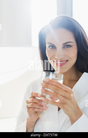 Portrait of smiling woman in bathrobe drinking water Banque D'Images