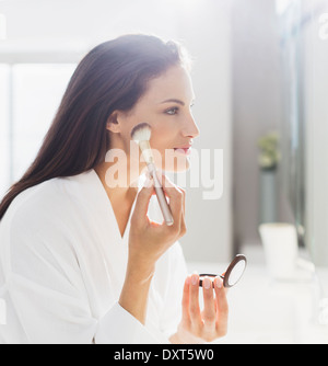 Femme en peignoir appliquant le maquillage dans la salle de bains Banque D'Images