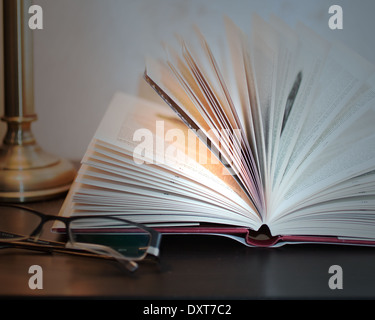Lunettes et livre ouvert sur une table de chevet Banque D'Images