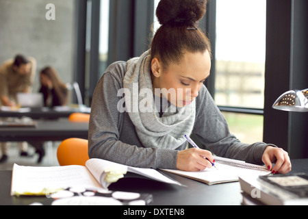 Étudiante à prendre des notes à partir de livres pour son étude. Young african american woman sitting at table avec des livres d'information. Banque D'Images