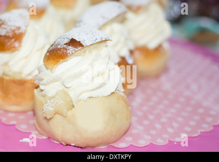 Petits pains suédois typique en février - semla - avec de la crème fouettée sur du papier à points rose et blanc et rose cakeplate. Banque D'Images