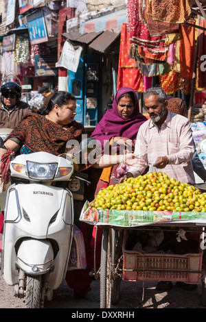 L'Inde, Dehradun. Femme sur moto acheter des fruits à un vendeur de rue. Banque D'Images