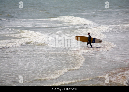 Entrer dans la mer surfer holding planche de surf à la plage de Bournemouth en Mars Banque D'Images