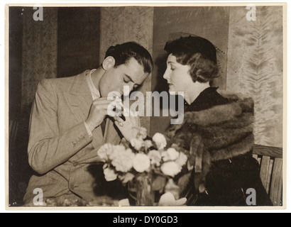 Cette photographie des années 1930 de Sam Hood capture un homme allumant une cigarette, une pratique sociale courante de l’époque. L'image reflète la mode et le style de vie de l'époque, ainsi que le moment historique capturé en noir et blanc. Banque D'Images