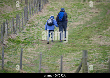 Un couple 2 deux personnes se tenant la main comme ils marchent en amont dans les champs, sur une balade. Vu de derrière. Banque D'Images