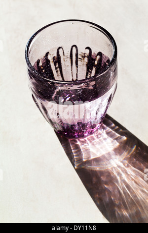 Verre à facettes violet avec de l'eau éclairée par la lumière du soleil Banque D'Images