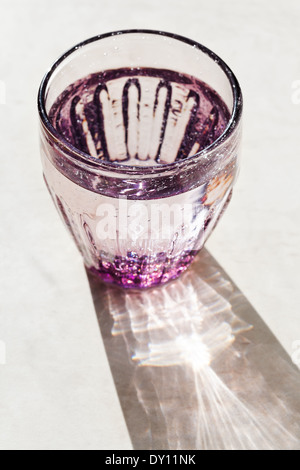 Verre à facettes violet avec de l'eau de source éclairée par la lumière du soleil Banque D'Images