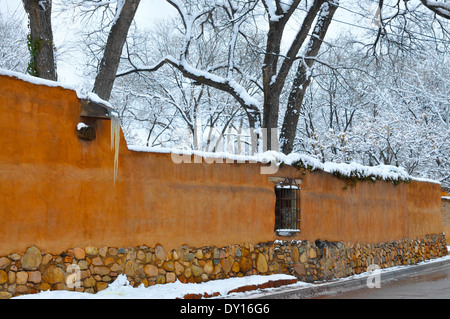 Adobe charmant est situé au sommet du mur de cour couverte de neige gainé cuir blanc agrémenté d'arbres, et de glaçons suspendus à un canale, Santa Fe NM Banque D'Images