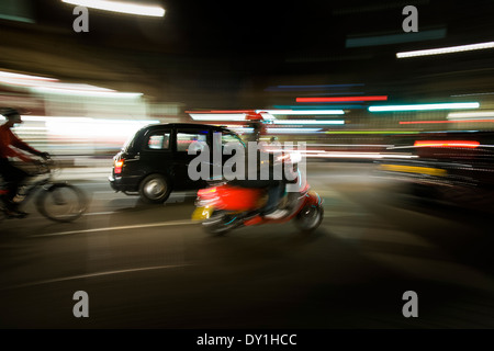 Un homme monte un scooter avec un taxi noir et taxi vélo, à travers la nuit l'heure de pointe à Londres. Banque D'Images