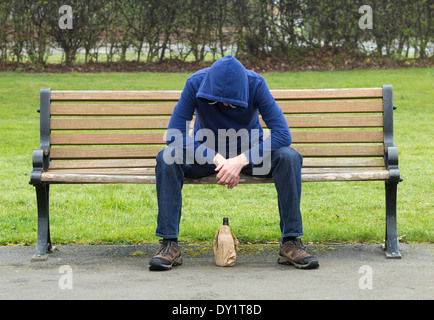 Homme portant des sweat assis sur banc de parc de boire de l'alcool Banque D'Images