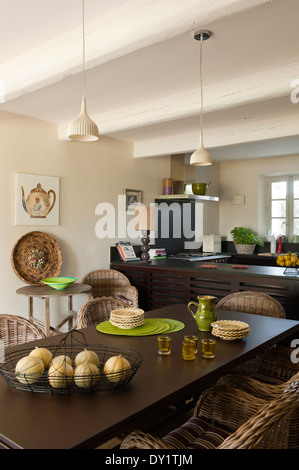 Chaises en rotin autour d'une table à manger en métal dans une cuisine traditionnelle avec des poutres au plafond, cuisinière Lacanche et bols de fil Banque D'Images