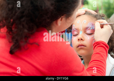 Petite fille de (6-7) est de faire son visage, peinture en plein air Banque D'Images