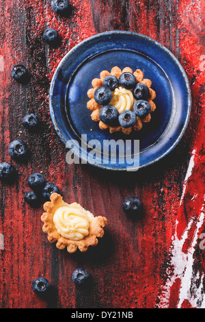 Vue de dessus sur le bleuet mini tartelettes servi sur une plaque en céramique bleu noir et rouge sur fond de bois. Banque D'Images