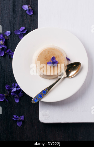 Vue de dessus sur la plaque avec pannacotta caramel servi avec des fleurs violettes sur fond noir et blanc Banque D'Images