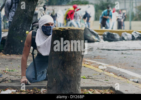 Caracas, Venezuela - le 3 avril 2014 : ouverture de se cache derrière un arbre et se prépare à lancer une roche à la Police nationale à une émeute à l'extérieur de l'Université centrale du Venezuela (UCV). Credit : Rafael A. Hernández/Pacific Press/Alamy Live News Banque D'Images