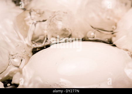 Des bulles apparaissent à la surface de l'eau bouillante comme quatre oeufs blancs sont cuits dans un pot Banque D'Images