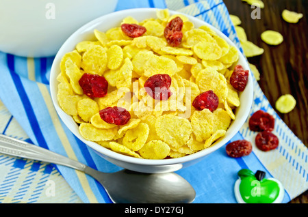 Flocons de maïs jaune avec les cerises séchées, le lait dans un pichet, cuillère, serviette sur l'arrière-plan de planches en bois Banque D'Images